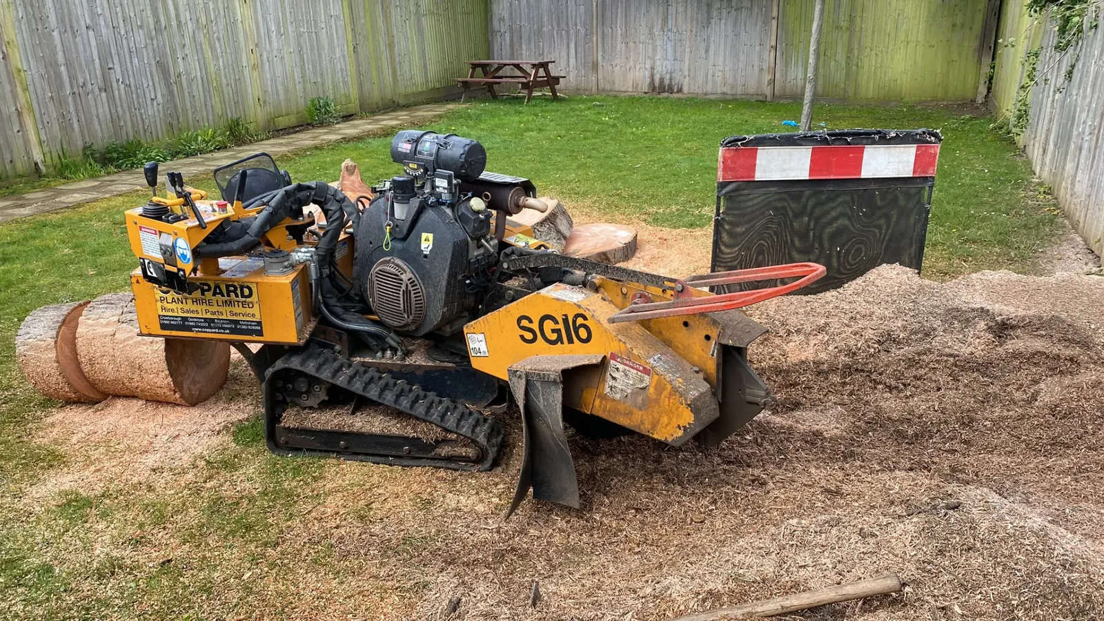 Tracked stump grinder on a lawn grinding a tree stump out below ground level